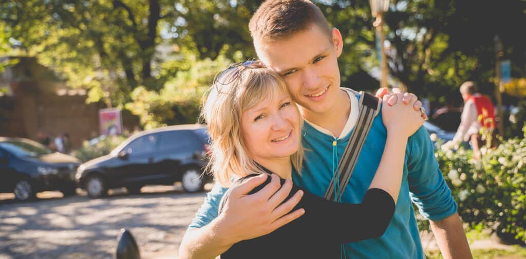 A woman and a teenage boy embrace outdoors