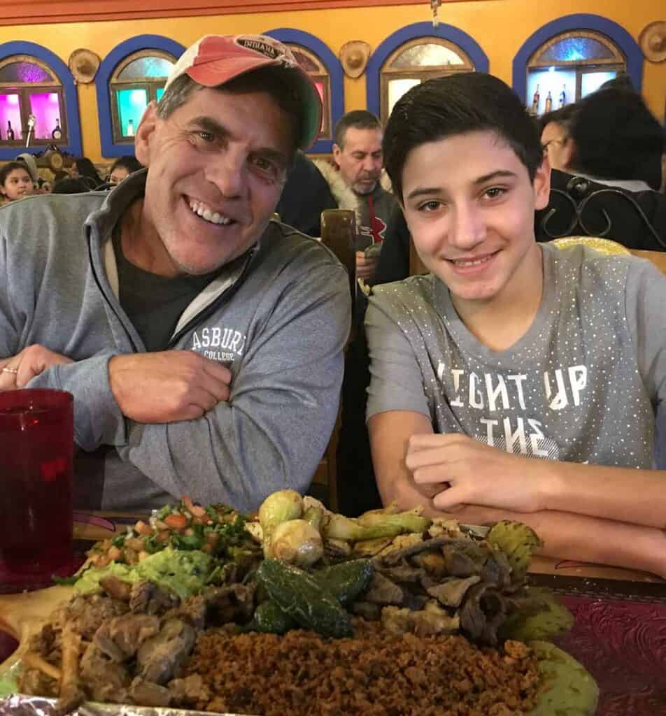 A man and teenager sit at a Mexican Restaurant with a plate of food before them.