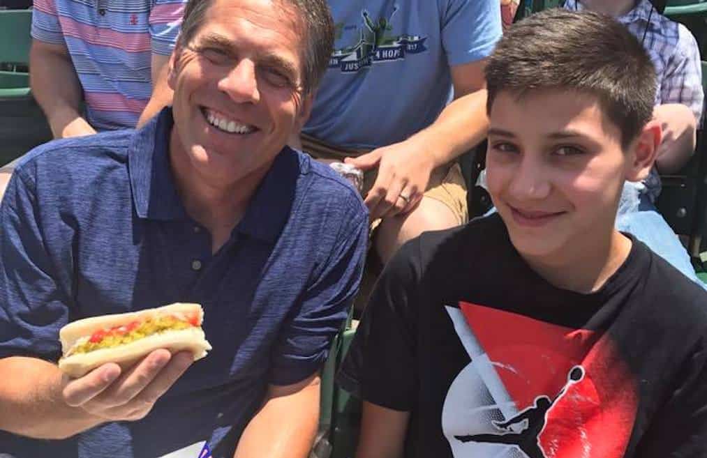 An adult mentor and young boy enjoy a hotdog at a baseball game.