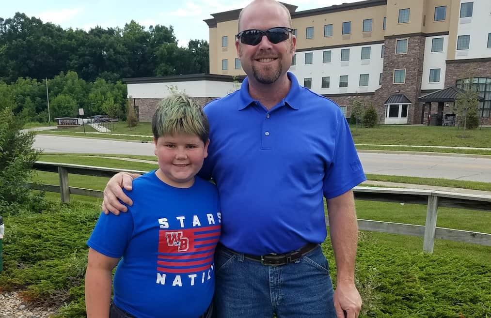 A young boy stands next to his adult mentor outside.