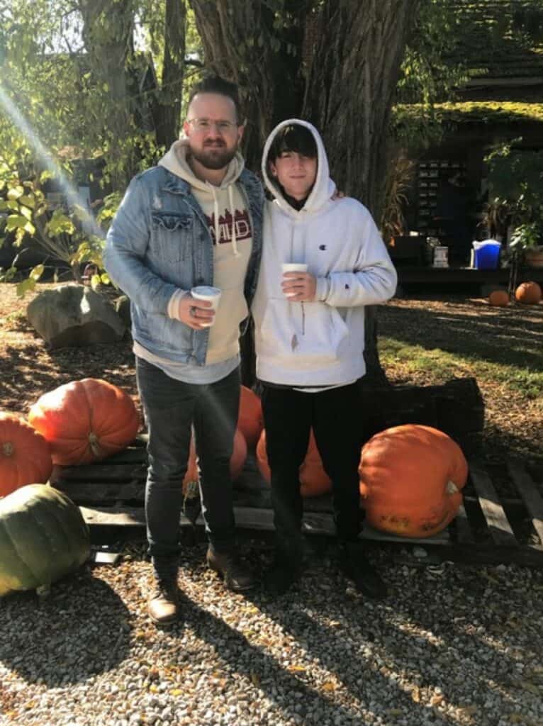 An adult mentor and teen hold cups of hot apple cider at a pumpkin patch.