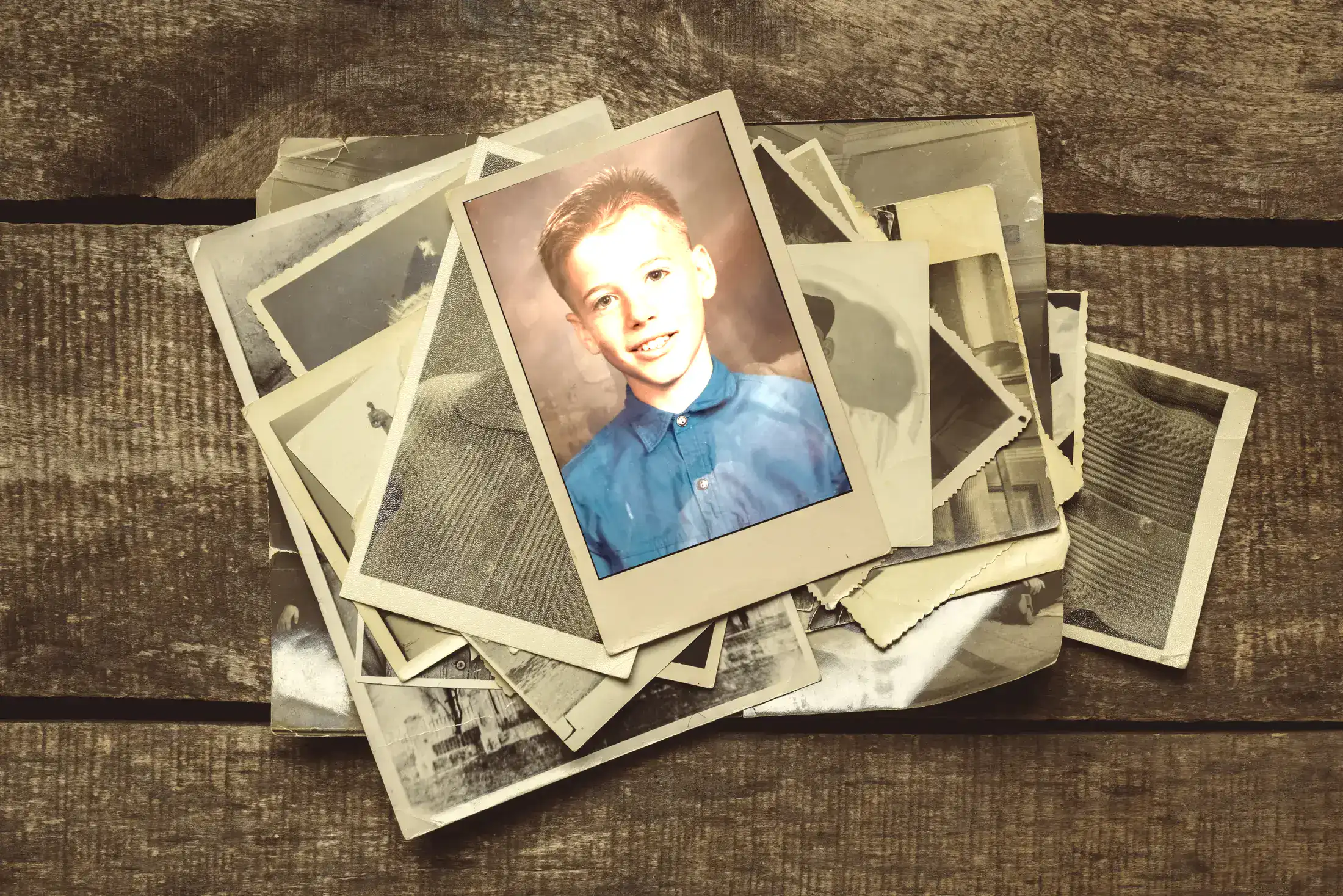 A pile of old family photographs on a wooden table, with young Matt's school picture on top