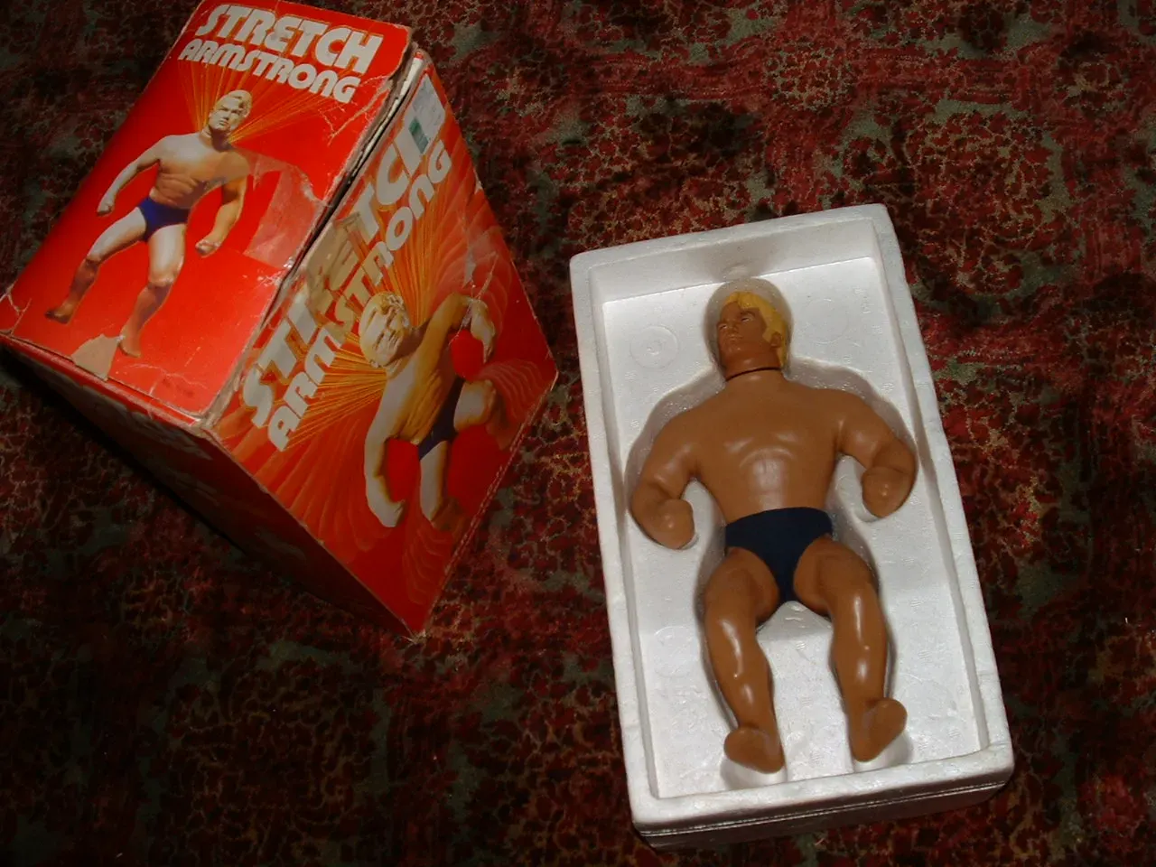 An original Stretch Armstrong toy in its foam tray next to the box
