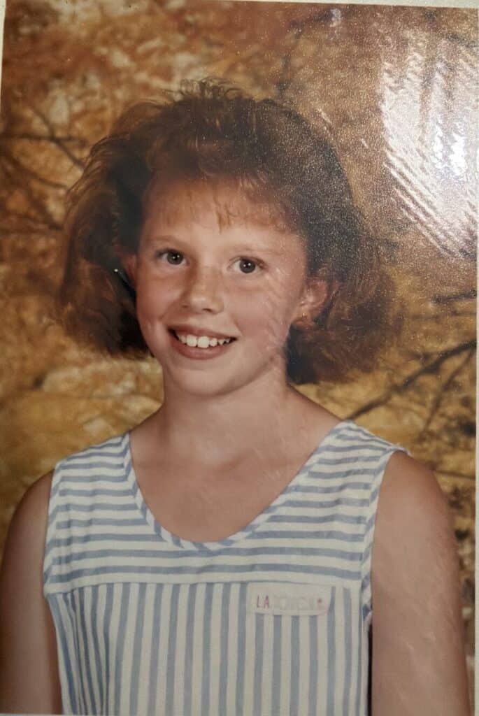 A school photo of a freckled girl with feathered hair in a striped top