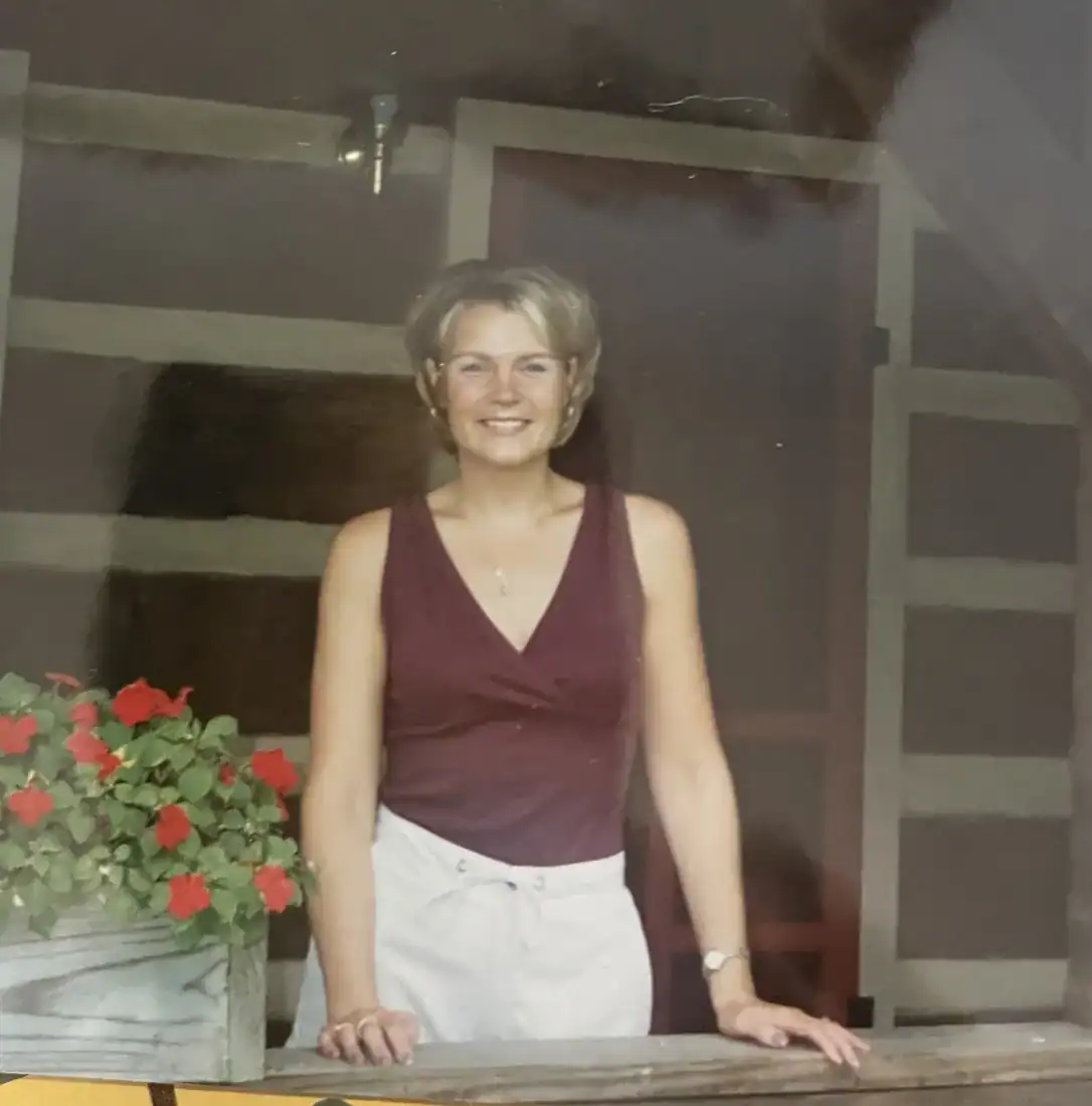 A young woman in a maroon top leaning on a porch rail beside red flowers