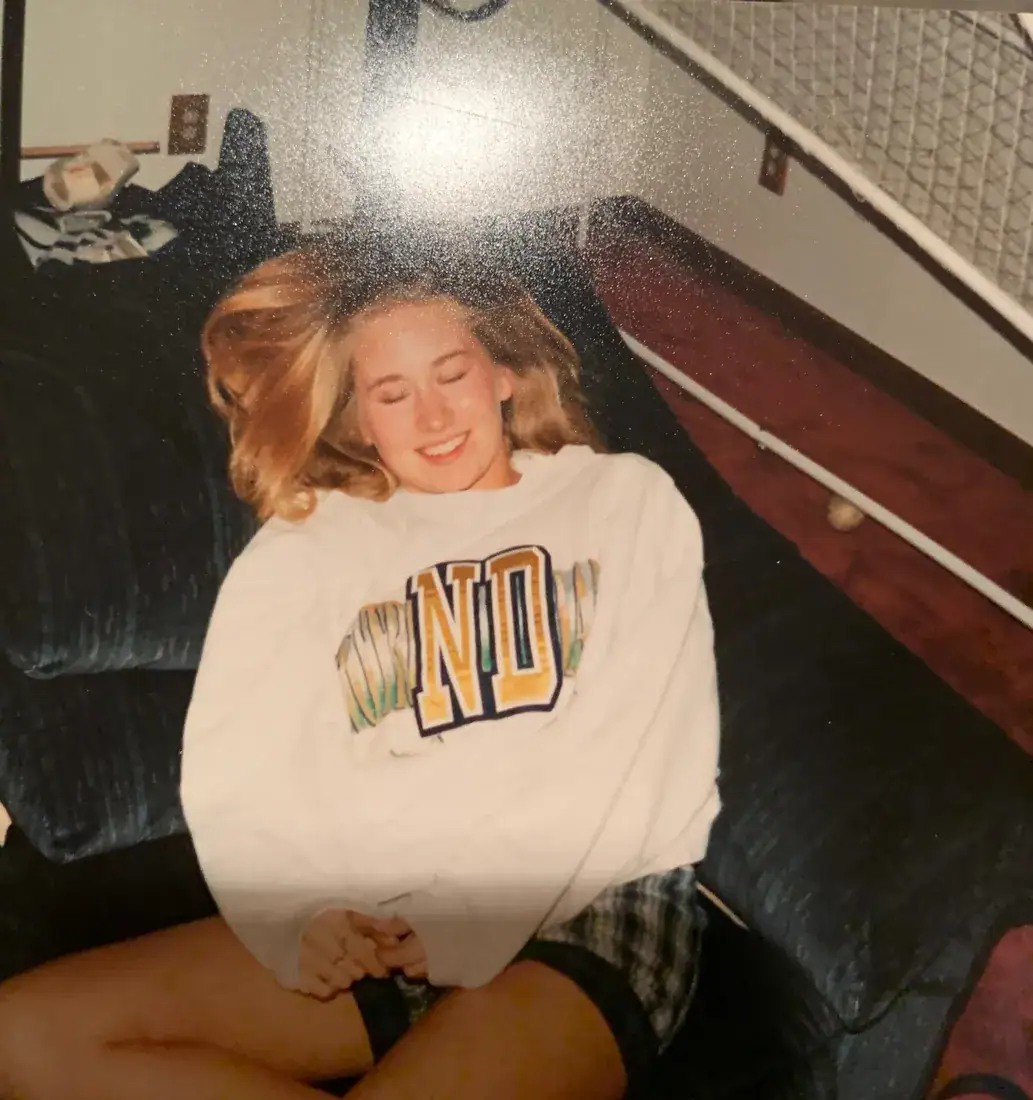 A teenager laughing on the couch in an oversized Notre Dame sweatshirt